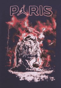 Laivaston t-paita, jossa on karhean pantterin graafinen kuva punavalkoisten salamoiden efektien keskellä, ja yllä on teksti "PARIS" sekä koripallologotipo.