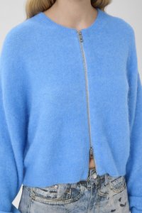 Hele sinine, pehme villasegune lukuga kampsun ümarate kaelusega ja langetatud õlgadega, kombineeritud kõrge vöökohaga tuhmunud teksapükstega.