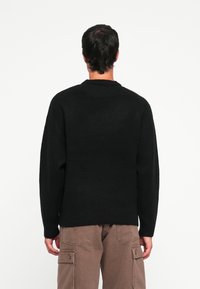 Zwarte gebreide trui met een ronde nek, losse pasvorm en lange mouwen, gecombineerd met beige cargo broek. Gelaagd stof, eenvoudig ontwerp.