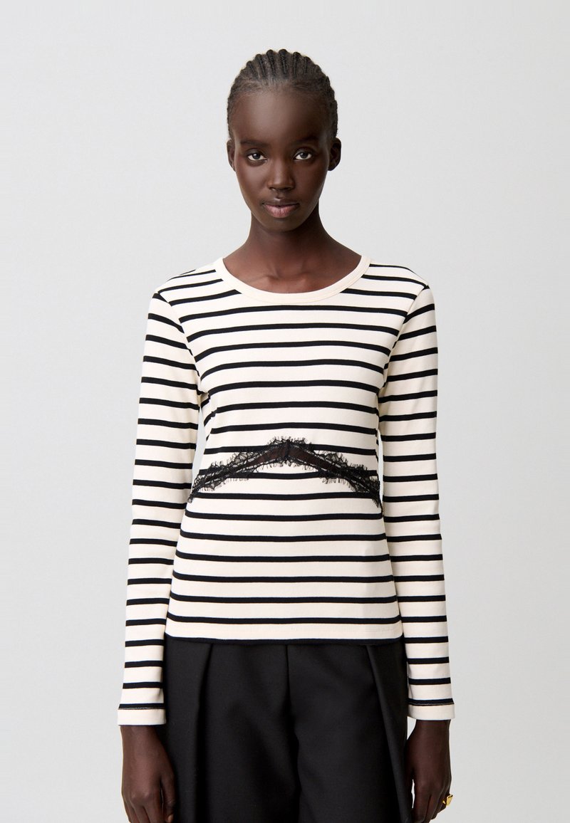Top de manga larga a rayas en crema y negro, con un detalle de encaje negro texturizado en la cintura. Material suave con un cuello redondo clásico.