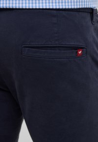 Navy Slim-Fit-Hose mit einer Gesäßtasche, die ein rot-weißes Markenetikett trägt, hergestellt aus glattem Baumwollstoff.