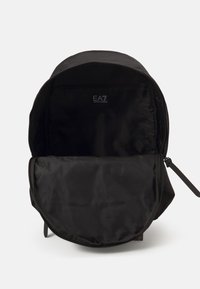 Zaino in nylon nero con forma arrotondata e chiusura a zip. L'interno presenta un logo e un ampio scomparto con tasca con zip.