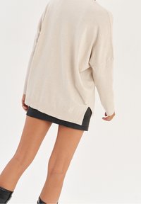 Beige oversized tröja med nedhasade axlar, ribbat nederkant och sidöppningar, matchad med en svart fusk läderkjol. Slät textur.