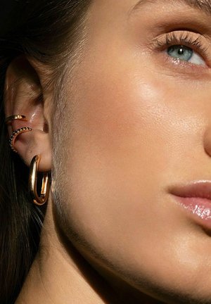 Guldringar och flera öroncuffar i minimalistisk design; slät, glänsande yta med textur av polerat metall.