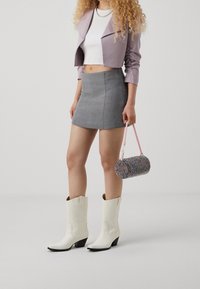 Botas de cowboy de cuero blancas, falda mini gris, chaqueta cropped lavanda y un bolso redondo de cuentas multicolor con un asa rosa.