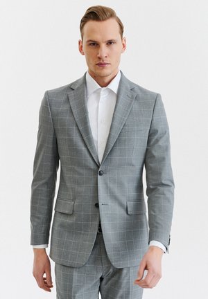 Szary w kratę garnitur z marynarką na dwa guziki i pasującymi spodniami. Posiada eleganckie klapy, boczne kieszenie oraz klasyczną białą koszulę pod spód.