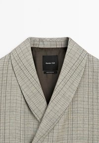 Grijs en beige geruite jas met een sjal kraag. Heeft een gestructureerde stof en een zwart binnenlabel met de tekst "Massimo Dutti, Made in Portugal."