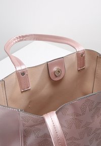 Ljusrosa läderhandväska med perforerat geometriskt mönster, med släta remmar och en tryckknappsstängning inuti.