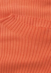 Geripptes Gewebe in leuchtendem Korallenorange mit vertikalen Streifen. Weiche Textur mit einem kleinen Taschendetail, das Elastizität und Wärme betont.