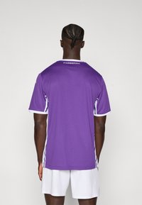 Maillot de sport violet avec des accents blancs et des manches courtes, présentant un tissu texturé et l'inscription "FIORENTINA" dans le haut du dos.