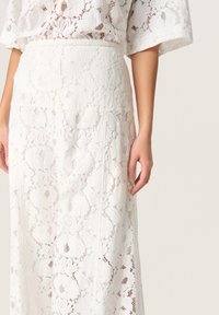 Weißer Spitzenrock mit floralen Mustern, hoher Taille und A-Linie. Die Textur ist durchsichtig und filigran mit sichtbaren Nähdetails.