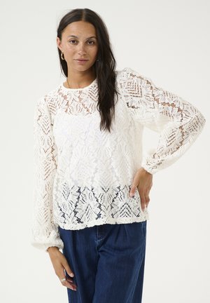 White lace blouse with a floral pattern, long puff sleeves, and a round neckline, paired with dark denim pants. Intricate textured design.