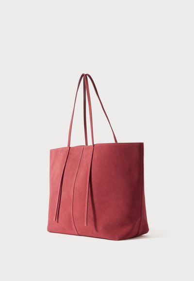 Red suede tote bag with two elongated handles, has a minimalist design featuring a smooth texture and subtle vertical seam details.