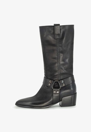 Stivale in pelle nera fino al ginocchio con punta appuntita, tacco medio e una cinghia decorativa con borchie metalliche e una fibbia circolare.