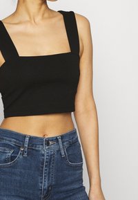 Crop top noir à larges bretelles, décolleté carré et texture côtelée, associé à un jean en denim bleu taille haute.