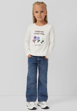 Camicia bianca a maniche lunghe con grafica floreale e testo "FOREVER TOGETHER", abbinata a jeans di denim blu larghi e sneakers bianche.