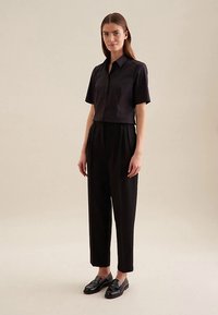 Czarna koszula na krótki rękaw z guzikami, zestawiona z czarnymi spodniami z wysokim stanem i czarnymi mokasynami. Gładka tkanina i dopasowany krój.