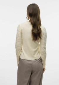 Roomwitte trui met textuur in beige mouwen met horizontale strepen. De onderrand is iets cropped, wat mooi aansluit bij losse grijze broeken.
