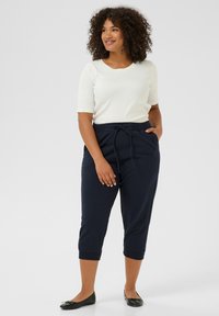 Pantaloni crop blu navy con vita elastica e cordoncino, abbinati a un top bianco a maniche corte. Modella che indossa scarpe nere basse, in piedi.