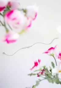 Bracelet en argent avec un design de feuille allongée, doté d'une chaîne délicate et d'un fermoir circulaire. Entouré de fleurs roses et blanches douces.