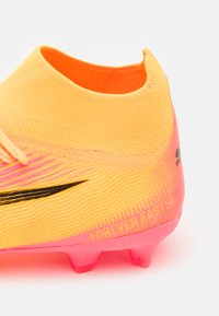 Scarpa da calcio gialla brillante con accenti rosa, superficie testurizzata e design elegante. Presenta un colletto lavorato a maglia e un logo nero sul lato.