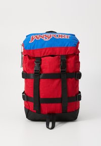 Sac à dos rouge avec un dessus bleu, doté de sangles et de boucles noires. Logo Jansport affiché en évidence sur le devant en lettres blanches.