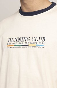 Hvit bomull t-skjorte med marineblå rund hals, med teksten "RUNNING CLUB" trykket i fet marineblå skrift og flerfargede linjer under teksten.