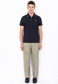Polo bleu marine avec bordure jaune, doté d'un col et d'une patte de boutonnage ; assorti à un pantalon cargo kaki et des chaussures noires.
