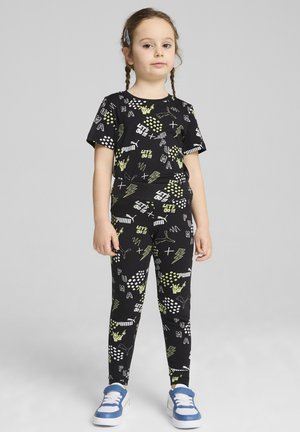 Zwart outfit met korte mouwen en leggings, bedekt met witte en groene grafische patronen. Gecombineerd met blauwe sneakers.
