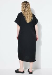 Vestido negro hasta la rodilla hecho de una tela ligera, con mangas cortas y un corte holgado. Presenta un patrón texturizado y acentos de abertura lateral.