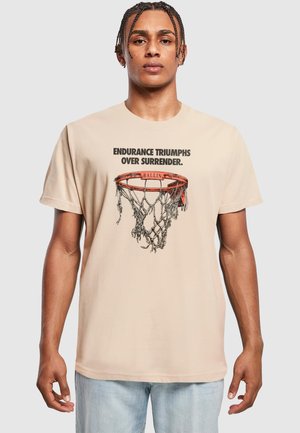 Beige t-skjorte med et grafisk motiv av en basketballkurv med nett. Teksten lyder: "UTHOLDENHET SEIER OVER OVERGIVELSE."