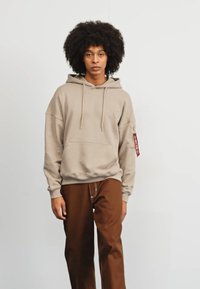 Felpa beige con cappuccio, tasca a marsupio e coulisse. Pantaloni marroni con una piacevole accentuazione in vita. Design minimalista e vestibilità rilassata.