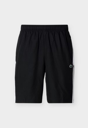 Mustat urheilushortsit, joissa valkoiset sivupaneelit ja joustava vyötärönauha, vasemmalla puolella pieni vihreä krokotiililogo.