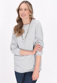 Maglietta a maniche lunghe grigio chiaro a coste con scollo rotondo e vestibilità leggermente comoda, abbinata a jeans in denim blu scuro. Design semplice e texture morbida.