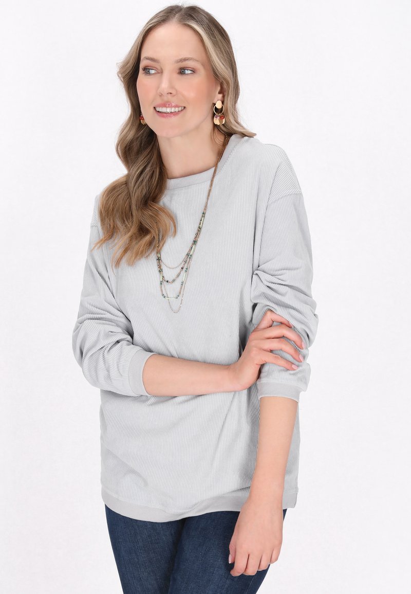 Maglietta a maniche lunghe grigio chiaro a coste con scollo rotondo e vestibilità leggermente comoda, abbinata a jeans in denim blu scuro. Design semplice e texture morbida.