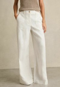 Weiße Leinenhose mit weitem Bein und hoher Taille, ausgestattet mit zwei Fronttaschen und einem Knopfverschluss. Glatte Textur und minimalistisches Design.