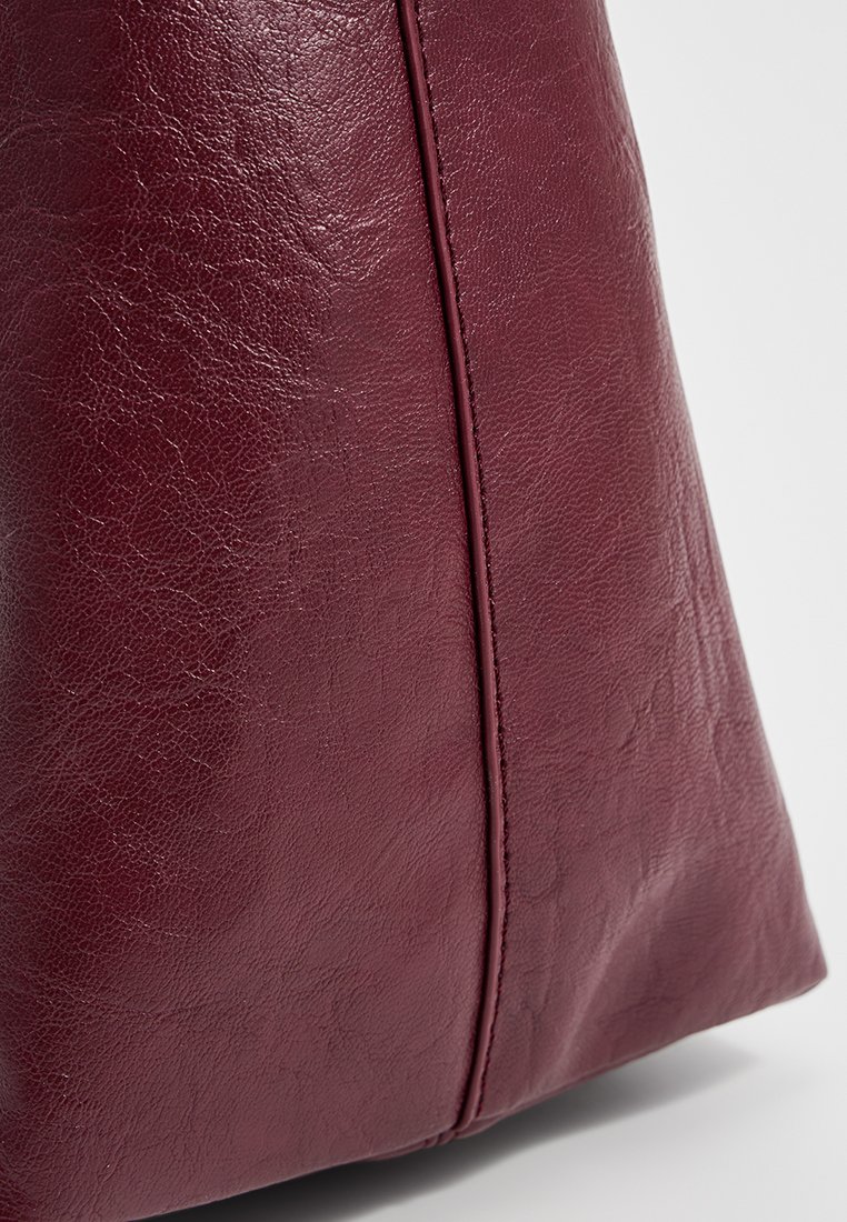 Bolso de piel burdeos con un acabado texturizado, que presenta un ligero brillo, un detalle de costura vertical y una forma estructurada.