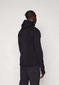 Black hoodie with a fitted design, textured fabric, a rounded hem, and a structured hood. The garment has contrasting stitching details.