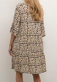 Zwart- en roomkleurige jurk met patroon, voorzien van een gelaagd ontwerp, ellebooglange mouwen en een zachte textuur. Achteraanzicht toont de volledige beweging.