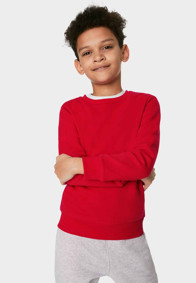 Roter Sweatshirt mit Rundhalsausschnitt und langen Ärmeln, mit einem weißen gerippten Kragen. Kombiniert mit hellgrauen Jogginghosen.