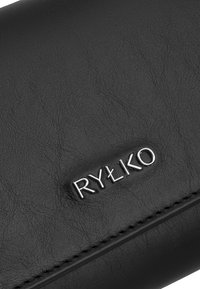 Portafoglio in pelle nera con una texture liscia, grana sottile e logo metallico in rilievo "RYŁKO" sul davanti. Dettagli di cucitura visibili.