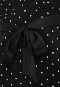 Svart kjole av stoff med hvite polkadotter. Fremhevet med en stoffsløyfe i livet, med en jevn, myk tekstur.