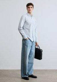 Vaaleansininen nappipaita, löysät vaaleat farkut, mustat nahkakengät ja musta salkku. Minimalistinen muotoilu rentoon istuvuuteen.