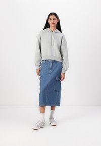 Sudadera gris de corte relajado con cordones, combinada con una falda midi de mezclilla azul que presenta bolsillos de carga, acompañada de zapatillas blancas.