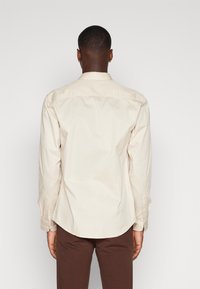 Light beige long-sleeve shirt with a classic collar, buttoned cuffs, and a curved hem. Smooth cotton fabric with no visible patterns.
