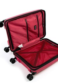 Červený kufr s tvrdou skořepinou, vybavený zipem. Uvnitř jsou dvě síťované kapsy a křížový popruh pro upevnění předmětů. Čtyři kola.