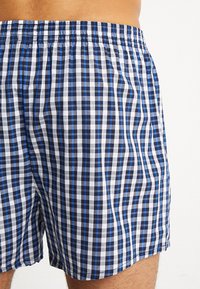 Boxer shorts dans un motif à carreaux bleu, noir et blanc. Fabriqués en tissu léger avec une ceinture élastique pour le confort.