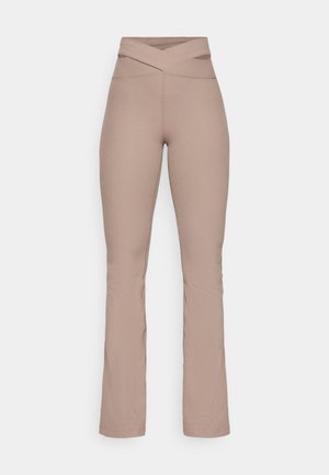 Calças beige com pregas e corte flare, com uma cintura cruzada alta. Textura suave e forma ajustada, estreitando-se do joelho à bainha. Detalhes de costura visíveis.