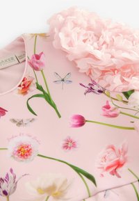 Kleid aus pinkem Stoff mit Blumenmuster, das verschiedene Blumen, Libellen und Schmetterlinge zeigt. Mit einer pinken Blumenruffle an der Schulter akzentuiert.