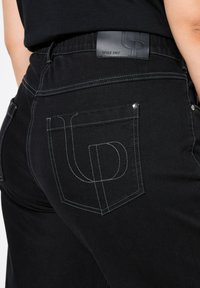 Černé džíny z denimu s hladkou texturou, úzkým střihem a kontrastním bílým prošíváním. Obsahují logo nášivku na pase.